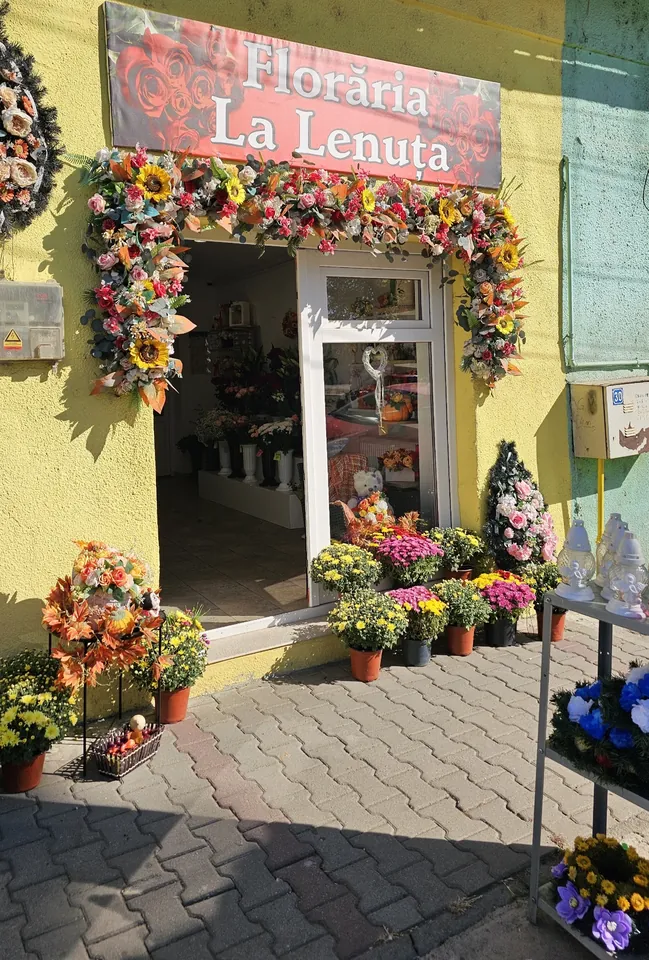 Florăria La Lenuța pe strada Tisei 29: fațada galbenă, firma roșie și ghirlanda de flori din jurul ușii